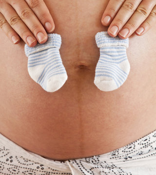 Pregnant woman holding blue baby socks on her tummy