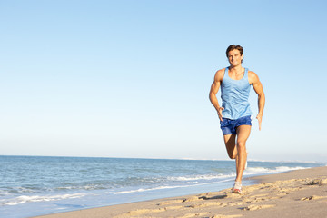 Fototapeta na wymiar Young Man In Fitness Clothing Running Along Beach