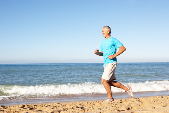 Senior Man In Fitness Clothing Running Along Beach