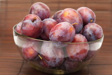 plums in a glass bowl on a bamboo mat