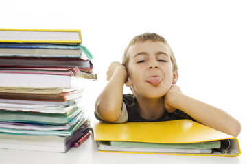 Child sticks out his tongue with school books on the table