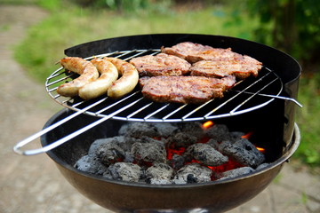 Grill mit Grillfleisch und Bratwurst im Garten