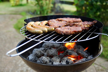 Grill mit Grillfleisch und Bratwurst im Garten