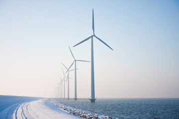 Row of snowy windmills standing in Dutch sea disappearing in win - obrazy, fototapety, plakaty