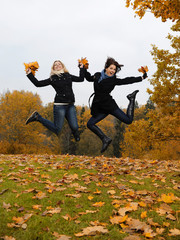 two beautiful girl friends with autumn leafs in a park jumping