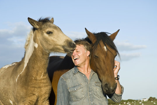 Happy Laughing Man Petting His Horse And Foal