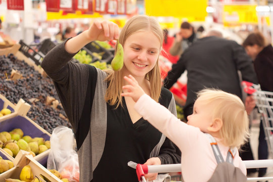 young mother and toddler girl shopping pear in supermarket