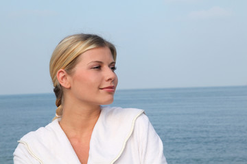 Smiling beautiful woman standing by the sea in bathrobe - obrazy, fototapety, plakaty