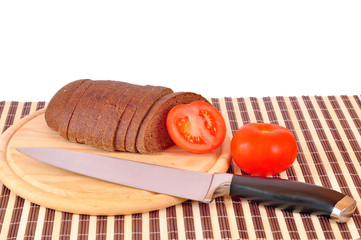 Rye bread on wooden board with knife and tomatoes
