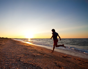 Teen boy runs at the beach on beautiful summer sunset