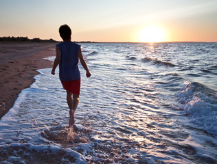 Teen boy runs at the beach on beautiful summer sunset
