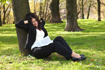 The businesswoman sitting on a grass, reading a book