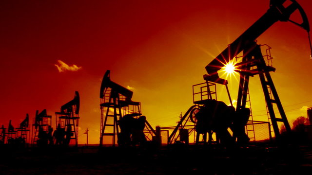 working oil pumps silhouette against sun