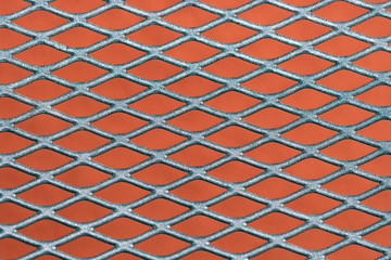 Abstract metal grating against red wall background