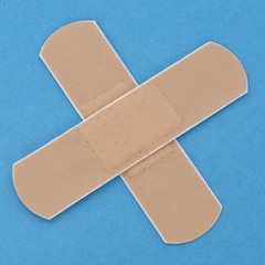 Two crossed adhesive bandages on blue background