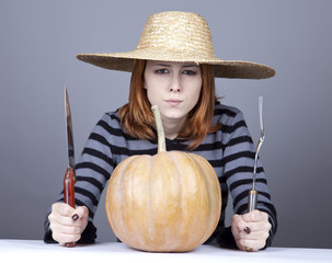 Funny girl in cap and fork with knife try to eat a pumpkin.