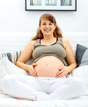 beautiful pregnant woman sitting on sofa and touching belly.