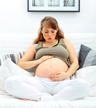 pregnant woman sitting on sofa and blowing kiss her belly.