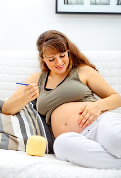 beautiful pregnant woman sitting on sofa and knitting for baby.