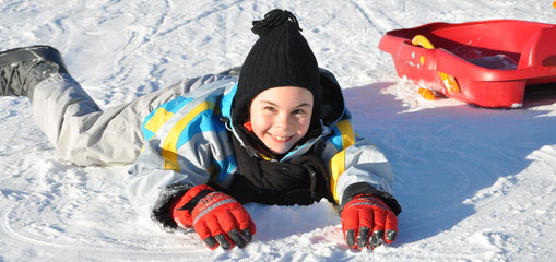 sport d'hiver fillette joyeuse couché sur la neige avec sa luge