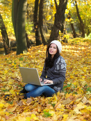 Beautiful woman working on laptop in park during autumn season