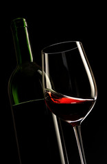 glass of red wine with a bottle and black background
