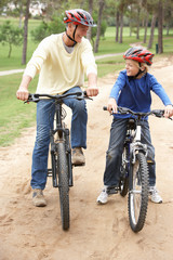 Obraz premium Grandfather and grandson riding bicycle in park