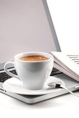 Hot cappuccino cup on laptop and newspaper