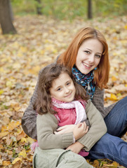 Fototapeta na wymiar Two sisters sitting on the leafs in the park.