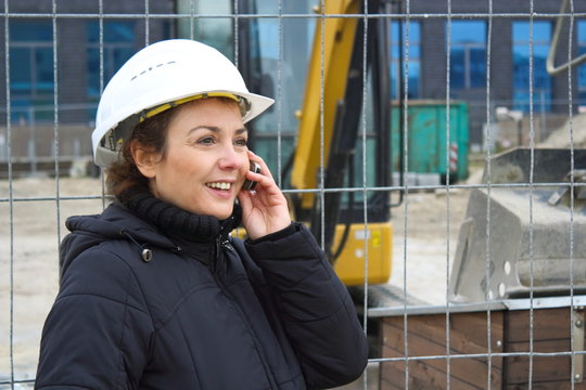 Bauleiterin telefoniert l&auml;chelnd auf einer Baustelle