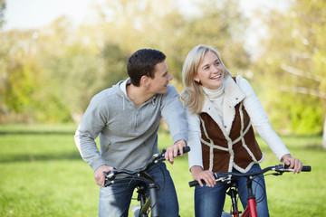 Fototapeta na wymiar Young happy couple in the park on bicycles