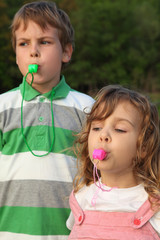 Beautiful small children, boy and girl, play with whistle