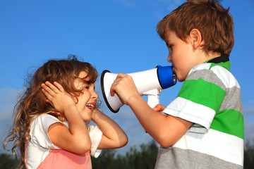 Small boy and girl play with loudspeaker, against blue sky