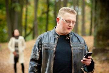 Fototapeta premium Man in park with girlfriend in background. Man call on phone