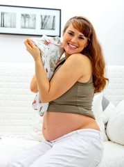 Smiling beautiful pregnant woman on sofa with baby clothes