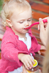 cute little girl outdoors in a park being fed apple purée by her