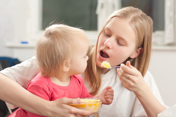 young adorable mother feeding his daughter with porridge