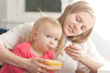 Obraz na płótnie Canvas young adorable mother feeding his daughter with porridge