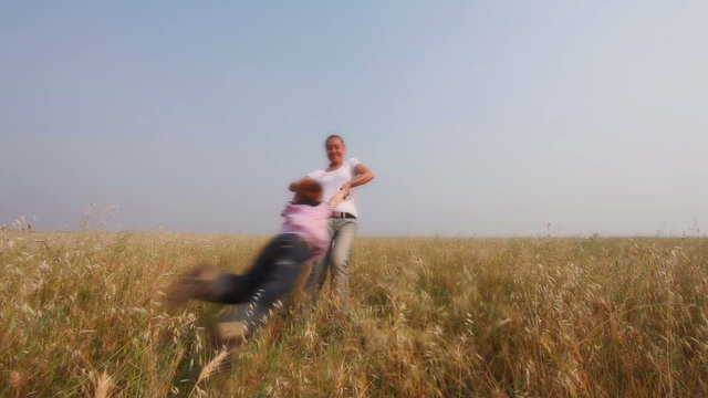 A young woman whirling her son in meadow