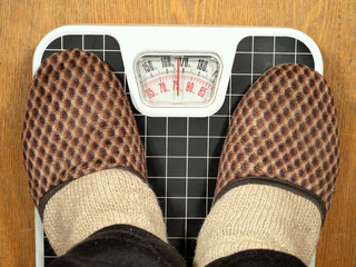Feet in slippers standing on floor scales. Scales indicate 75 kg