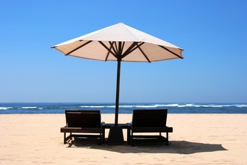 Два шезлонга под зонтом на песчаном берегу океана