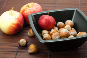 hazelnuts in a bowl and apples on a bamboo mat