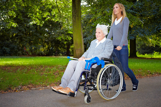Pflegerin fährt Rollstuhlfahrerin im Park