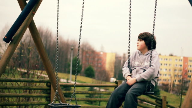 Young sad, lonely boy on a swing, dolly shot