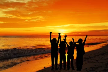 Fotobehang Childrens silhouettes on a sunset beach © Imagevixen