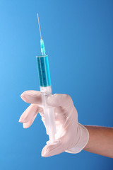 Syringe in doctors hand over blue background