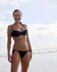 young woman wearing a bikini is standing at the beach