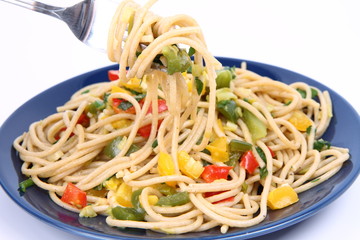 Spaghetti with vegetables being eaten with a fork on white