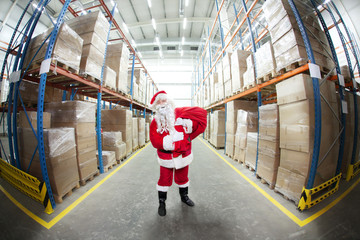 Santa Claus with red sack in storehouse full of presents - obrazy, fototapety, plakaty