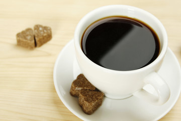 Closeup of a white cup of coffee next to lay pieces of sugar
